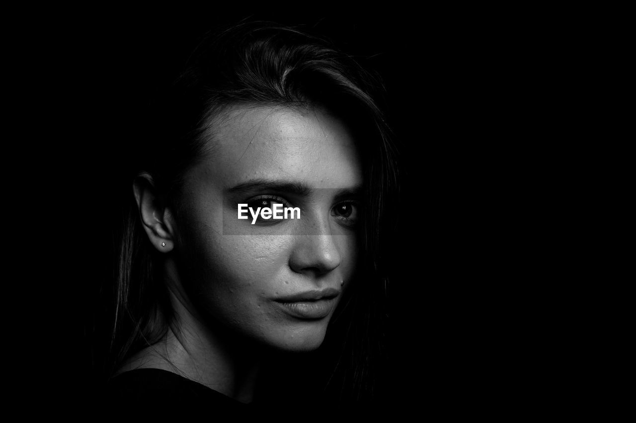 Close-up portrait of smiling young woman over black background