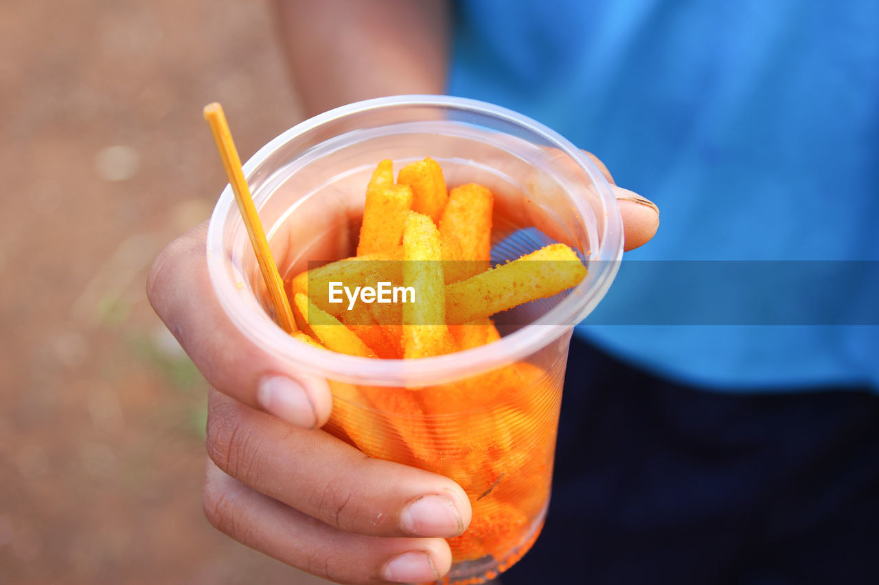 Midsection of person holding french fries in plastic glass