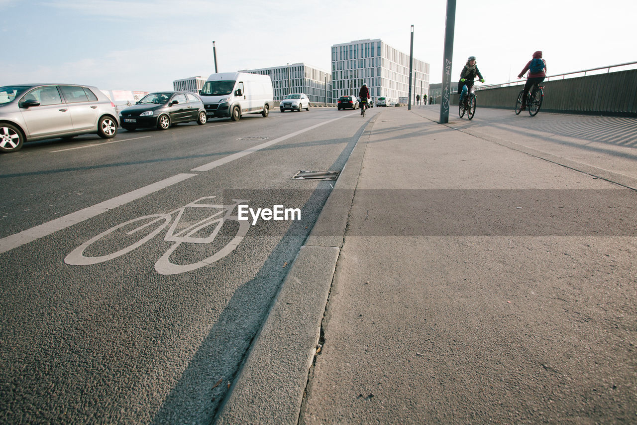 PEOPLE RIDING BICYCLE ON ROAD AGAINST SKY