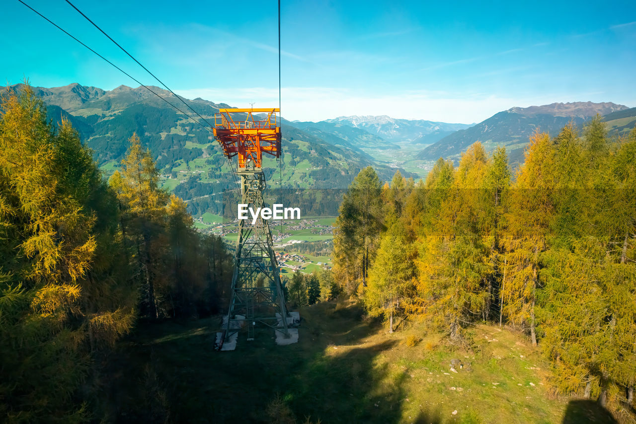 tree, mountain, scenics - nature, plant, nature, mountain range, beauty in nature, autumn, sky, landscape, cable car, land, environment, forest, pinaceae, cable, tranquil scene, coniferous tree, tranquility, overhead cable car, no people, wilderness, pine tree, travel, non-urban scene, leaf, day, outdoors, pine woodland, transportation, travel destinations, electricity, idyllic, valley, architecture, cloud, sunlight, yellow, woodland, green, technology, ridge, growth, reflection, tourism