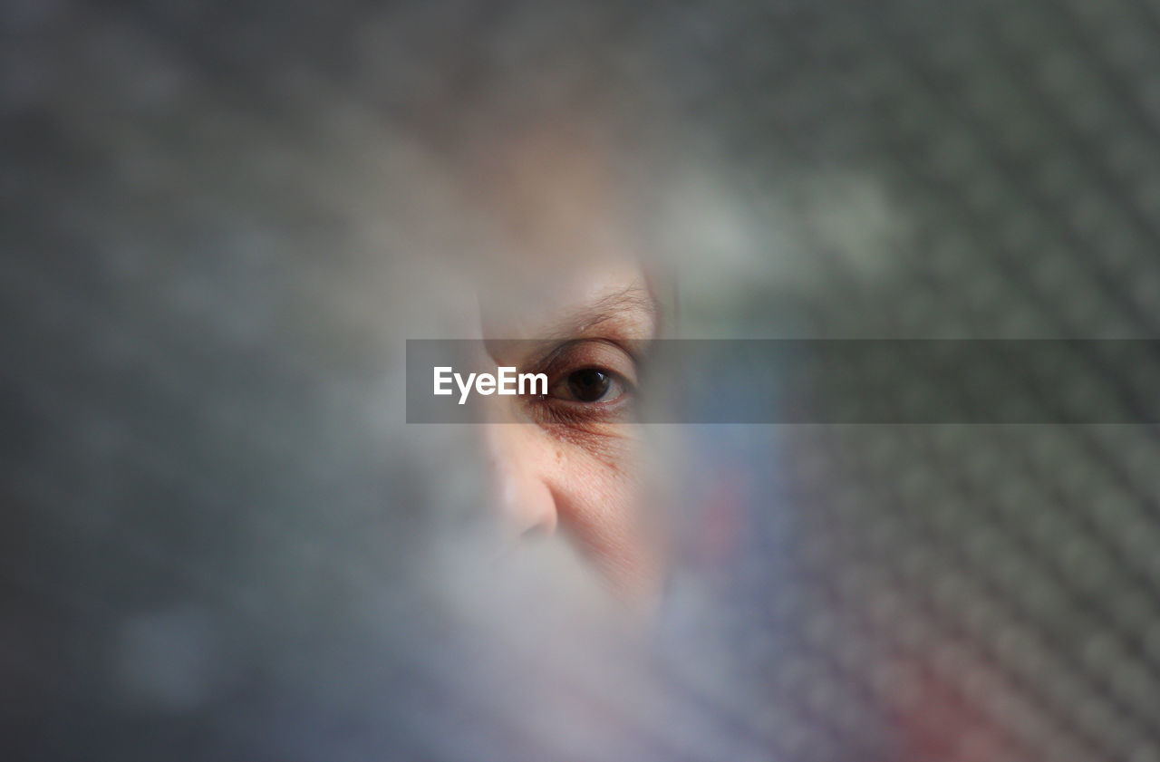 Close-up portrait of woman looking through broken glass