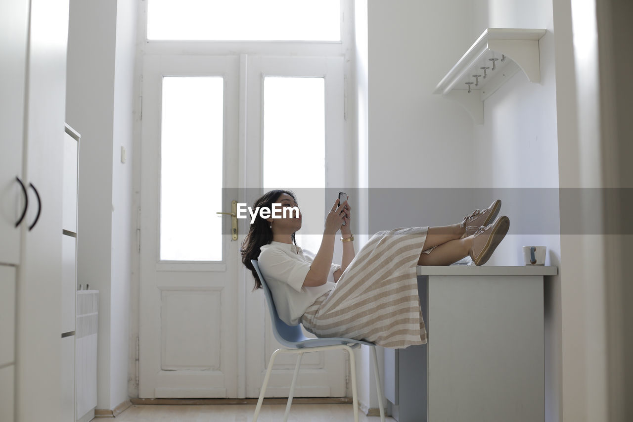 Woman using smart phone while sitting on chair at home