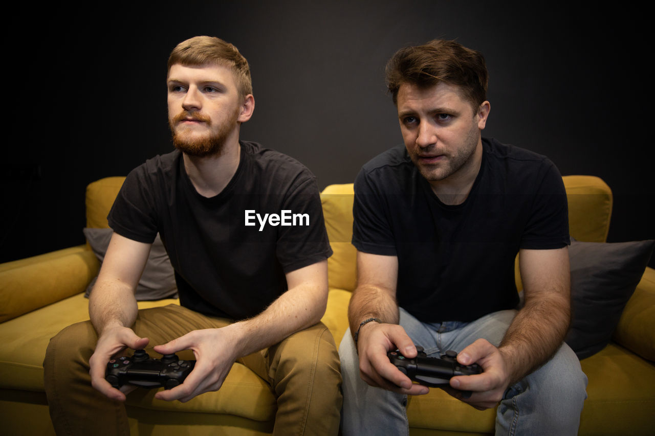 YOUNG MAN USING MOBILE PHONE WHILE SITTING ON SOFA AT HOME