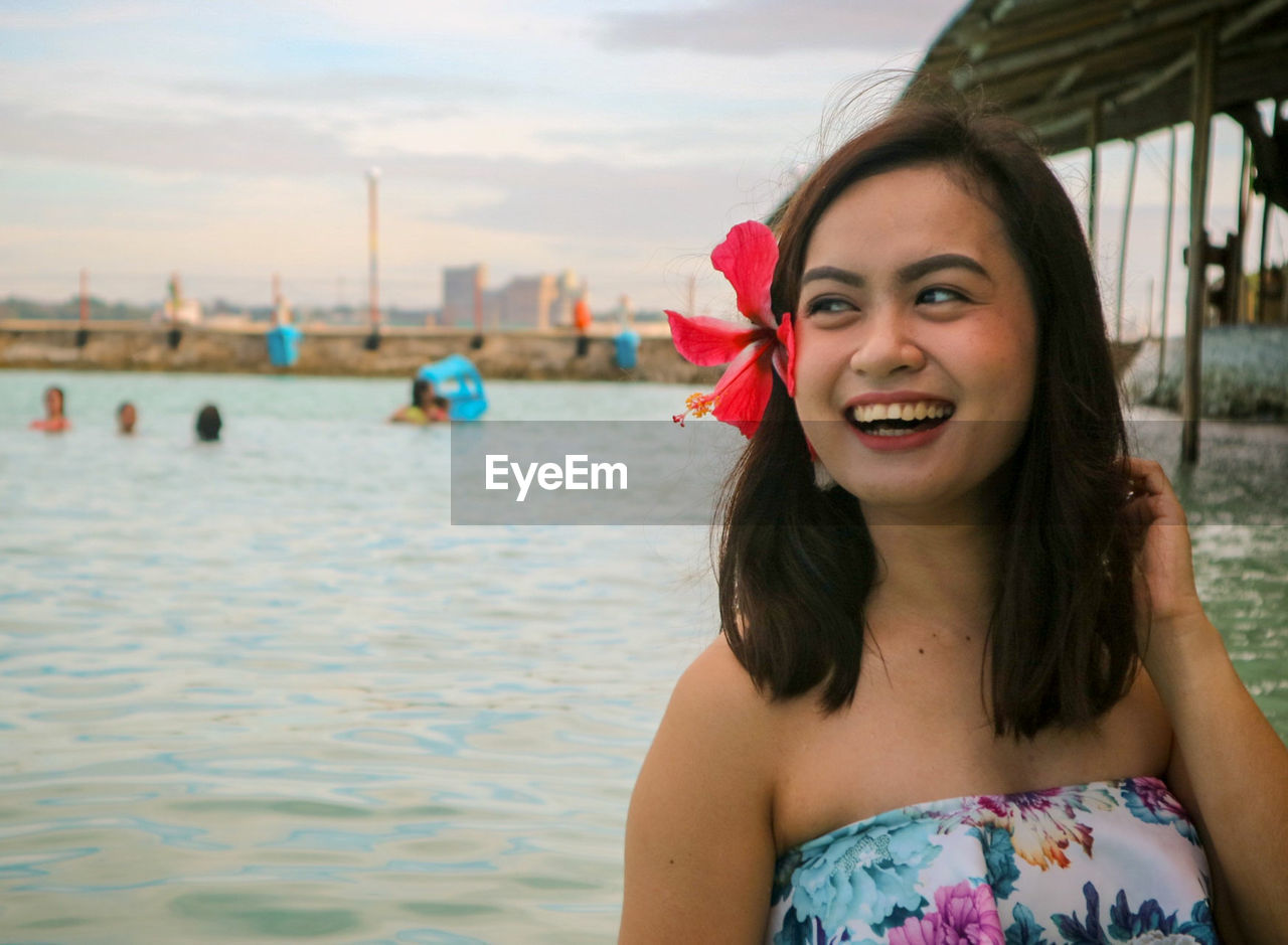 Cheerful young woman wearing flower looking away at beach