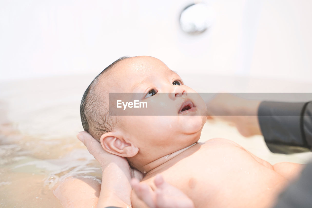 Midsection of mother bathing baby daughter in bathtub