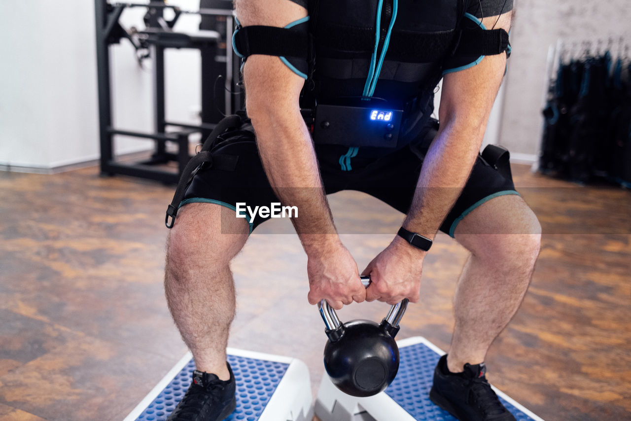 low section of man lifting dumbbell in gym