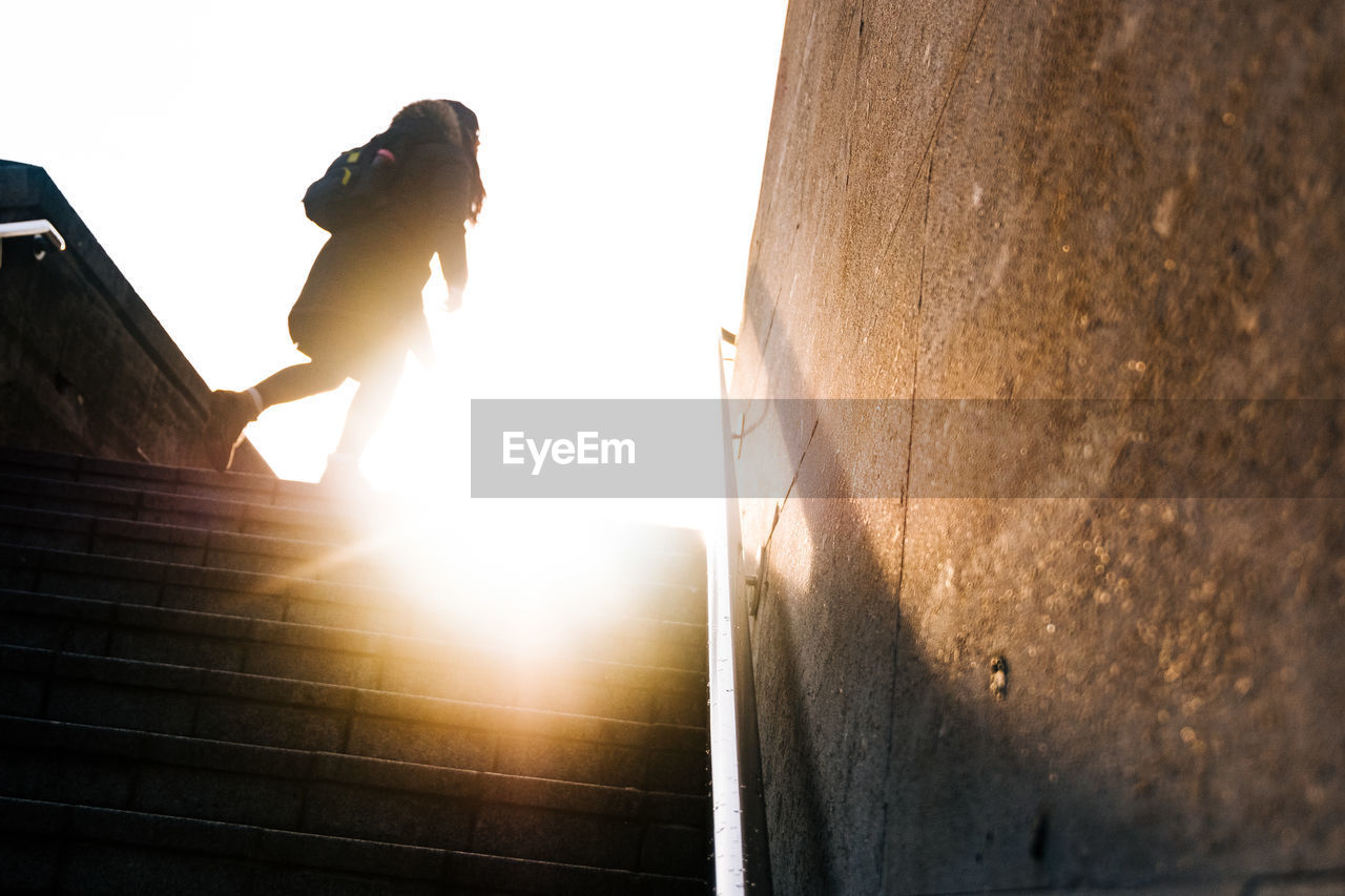 LOW ANGLE VIEW OF WOMAN STANDING ON STAIRCASE AGAINST SKY