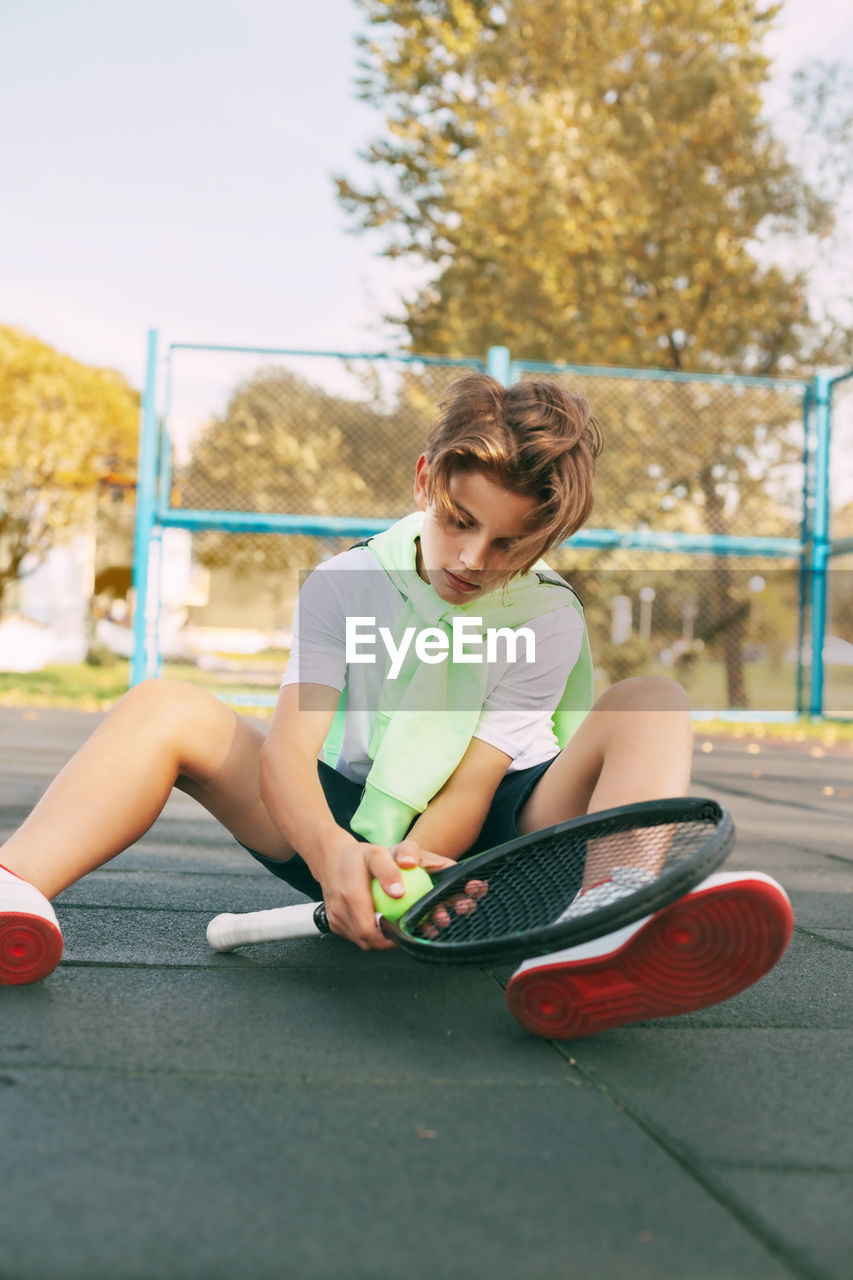 Beautiful teen athlete with a tennis racket in his hands. a tennis player sits on the court