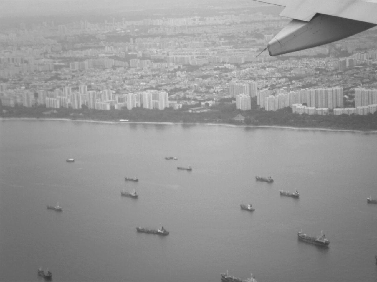water, architecture, transportation, city, aerial view, mode of transportation, building exterior, black and white, built structure, vehicle, monochrome, cityscape, nature, flying, monochrome photography, travel, no people, air vehicle, travel destinations, building, day, sky, high angle view, airplane, nautical vessel, landscape, outdoors, aircraft, aerial photography, sea, aircraft wing, environment, mid-air, urban skyline, business