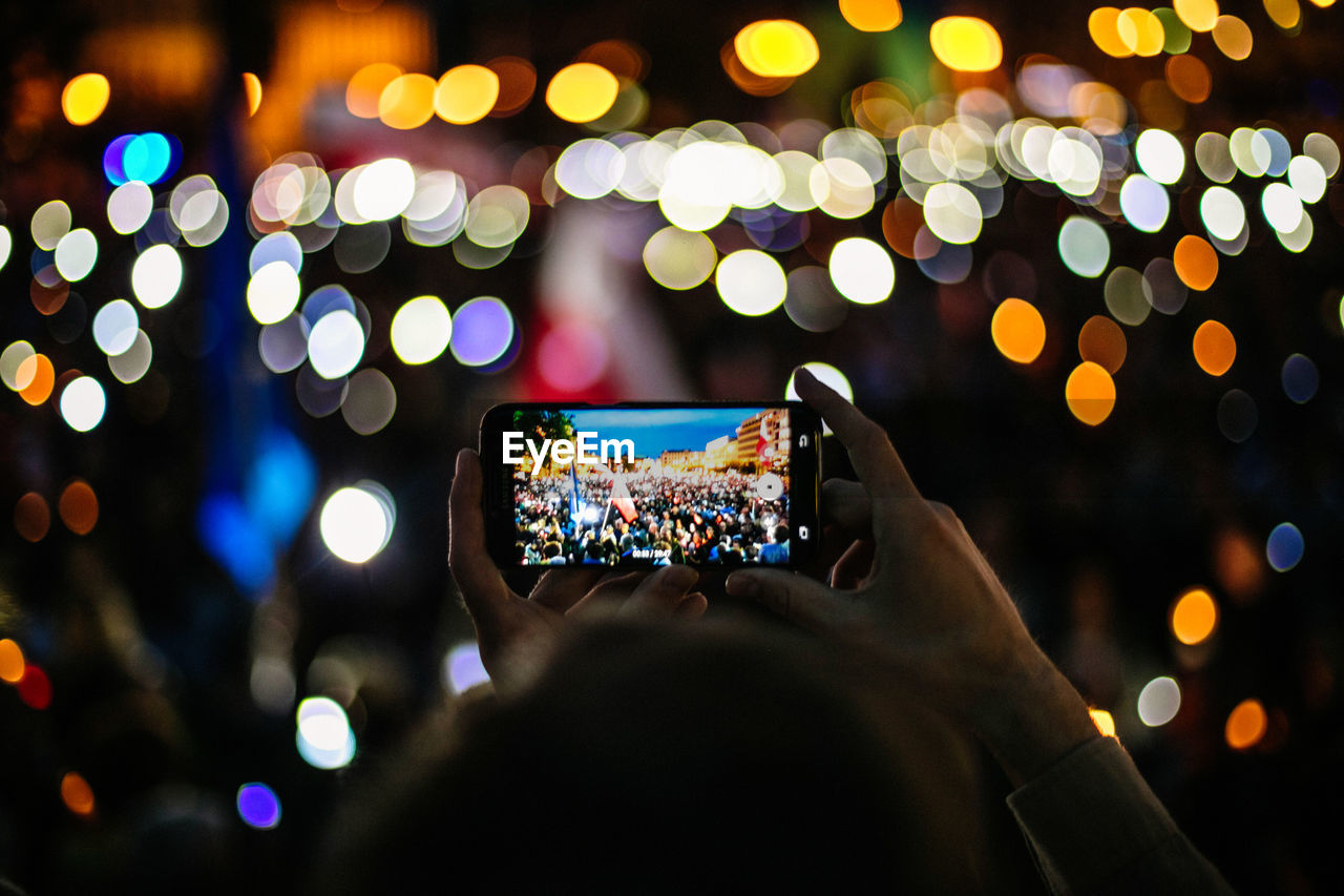 Cropped hands of man photographing illuminated protest at night