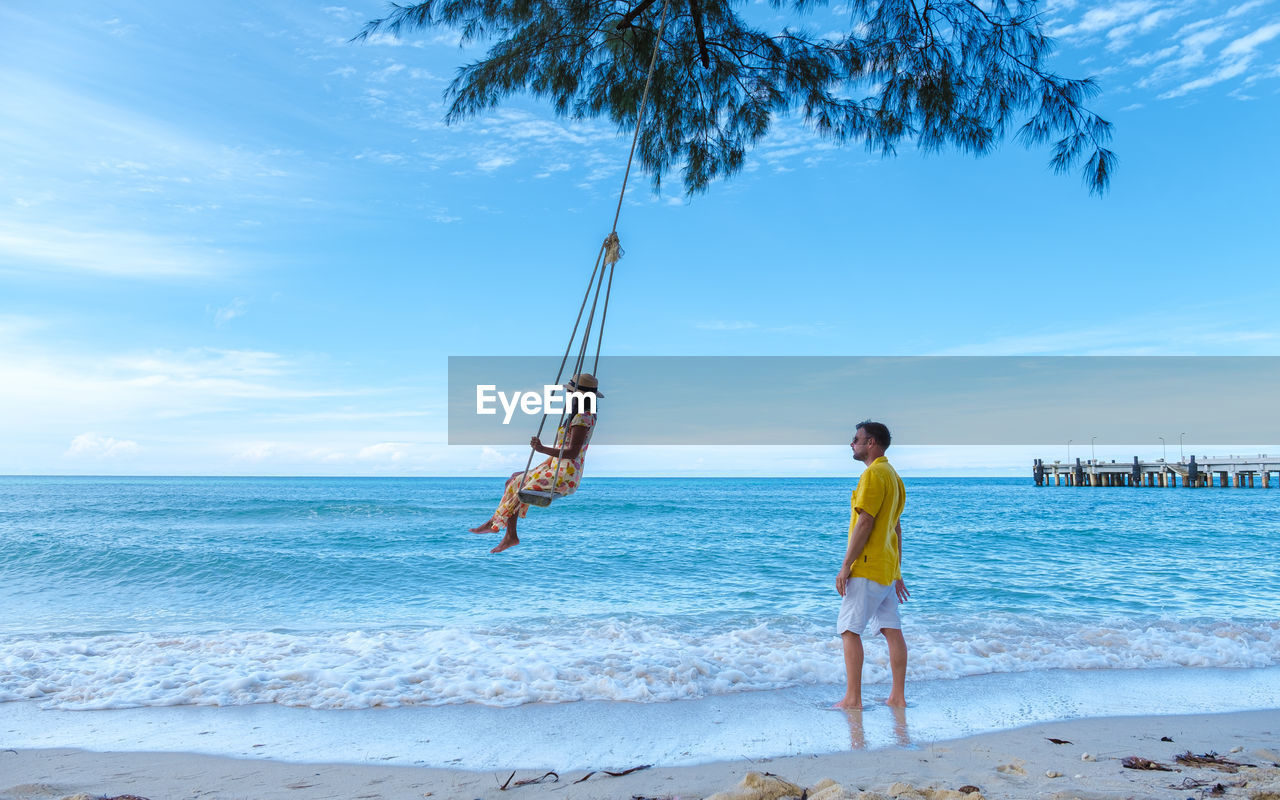 rear view of man standing at beach against sky