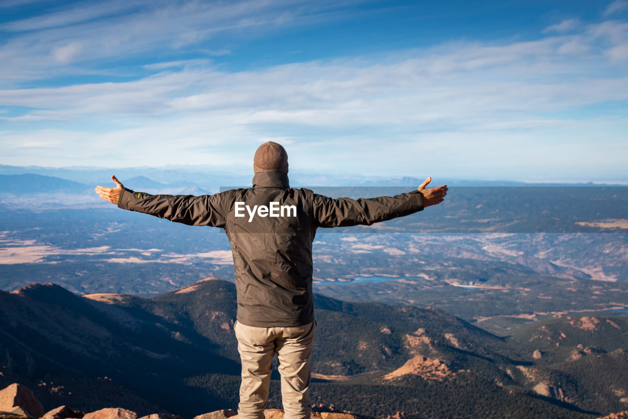Rear view of man standing on top of pikes peak, colorado with arms wide open against sky