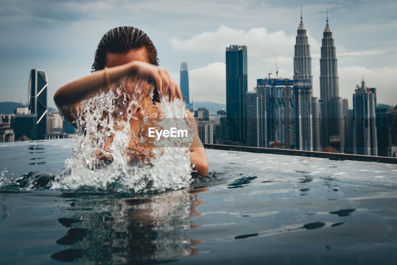 WOMAN IN SWIMMING POOL AGAINST BUILDINGS