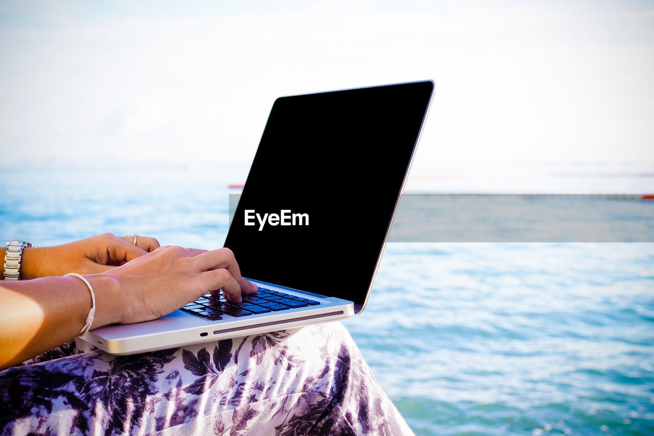 Midsection of person using laptop at sea