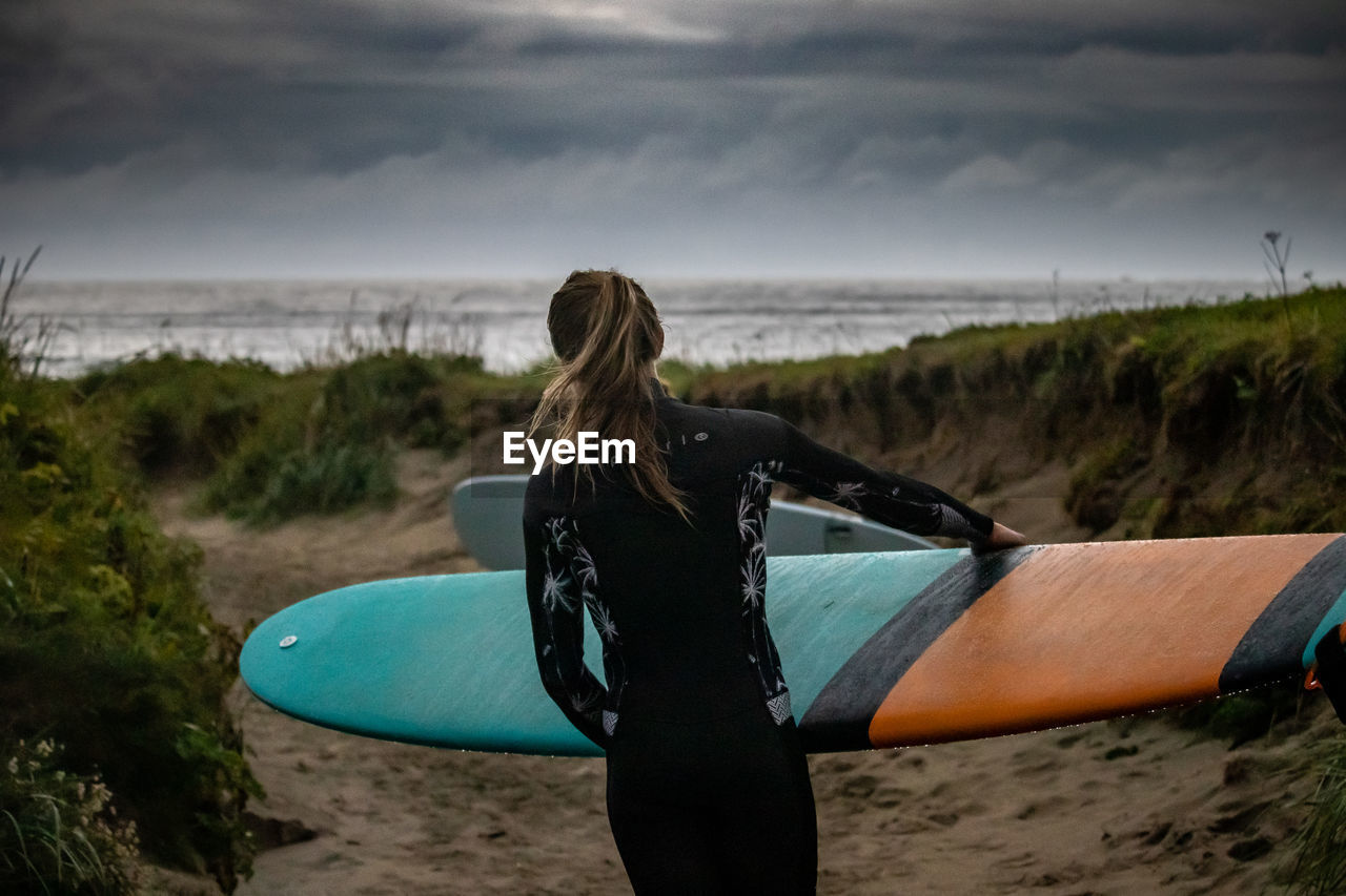 REAR VIEW OF WOMAN ON BEACH AGAINST SKY