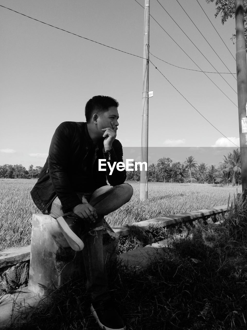 Full length of young man sitting on field against sky