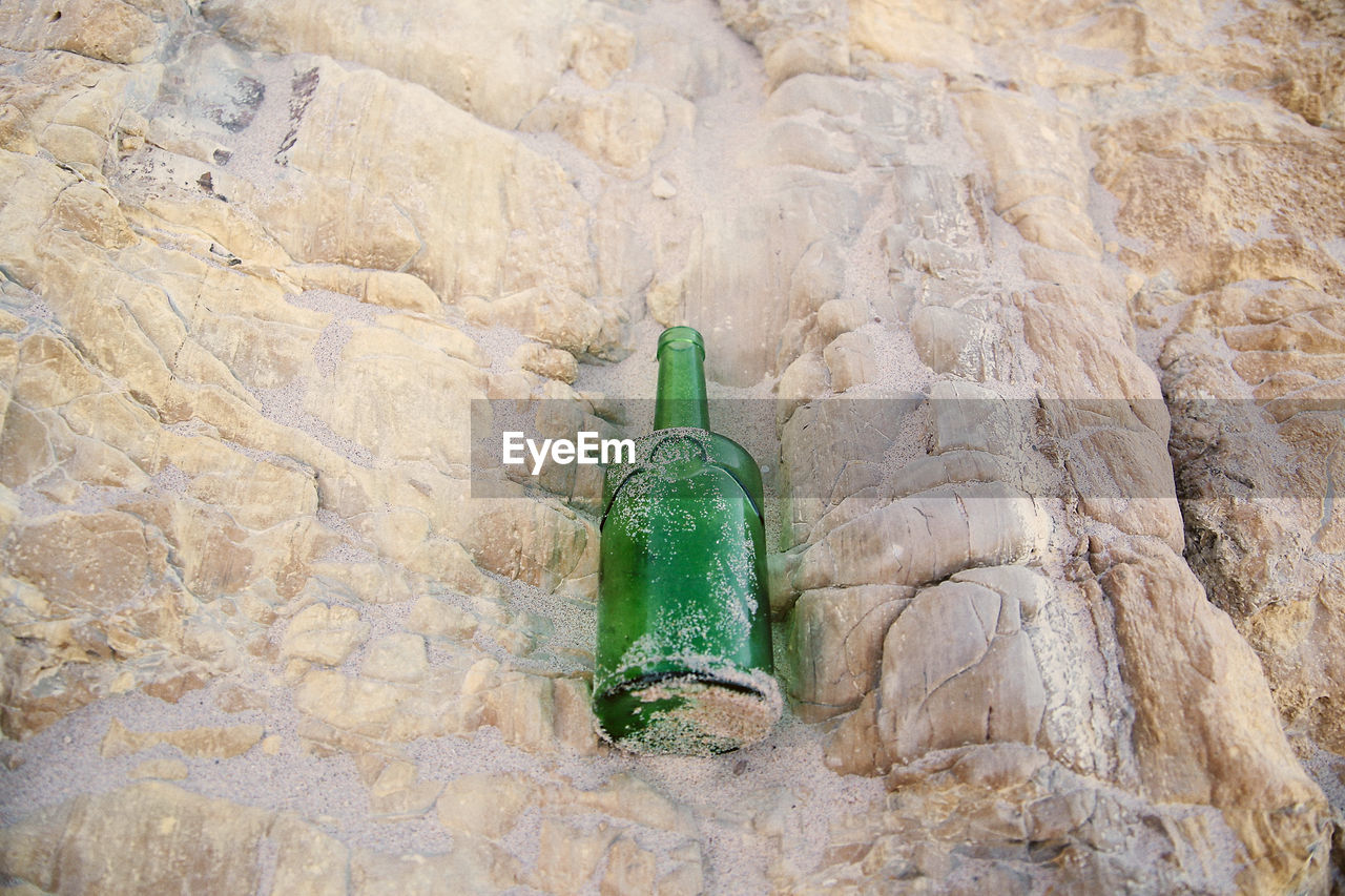 HIGH ANGLE VIEW OF BOTTLE ON ROCK