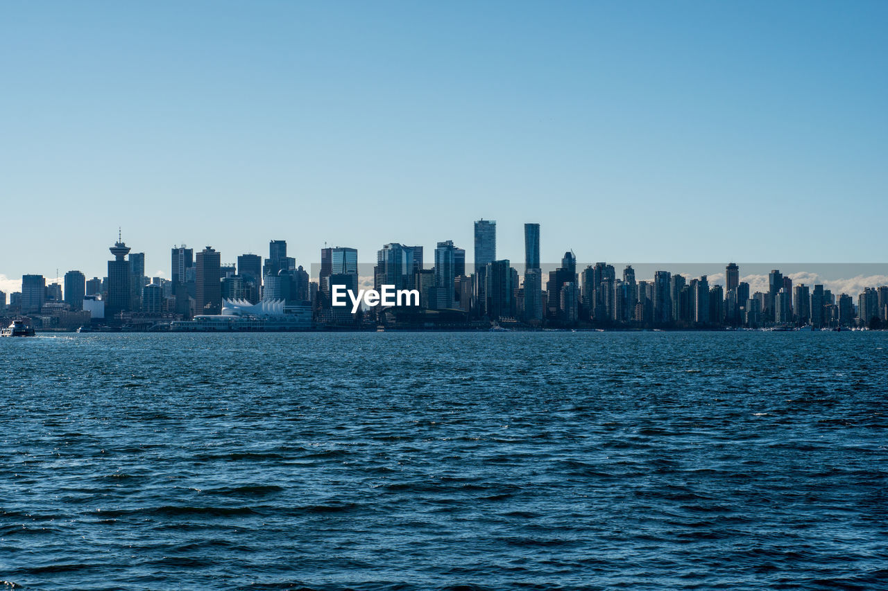 Sea by modern buildings against clear sky