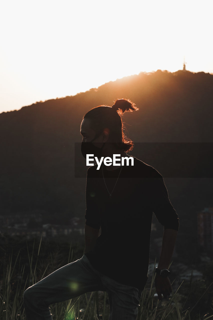 Young man standing on field against sky during sunset