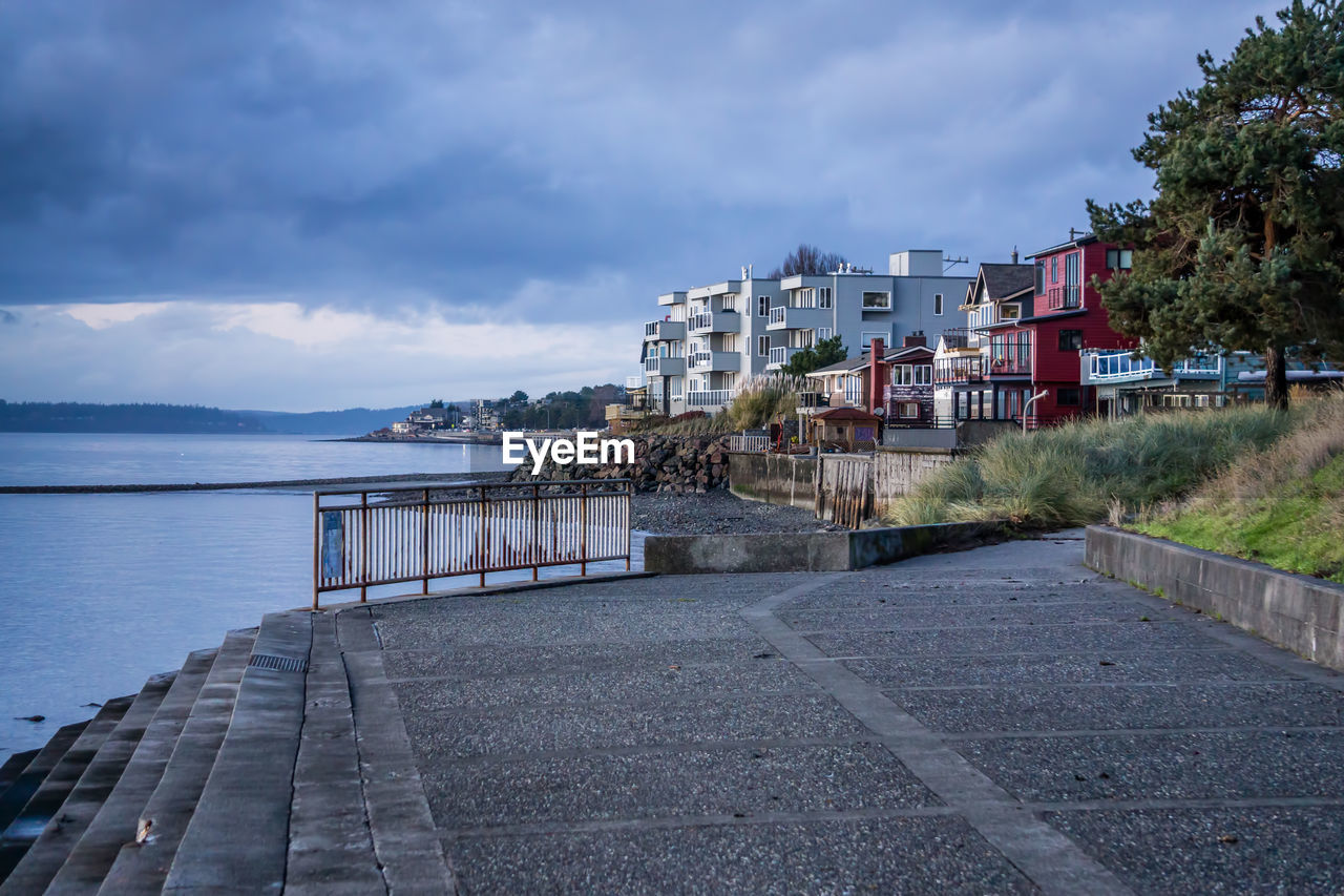 Footpath by sea against sky in city