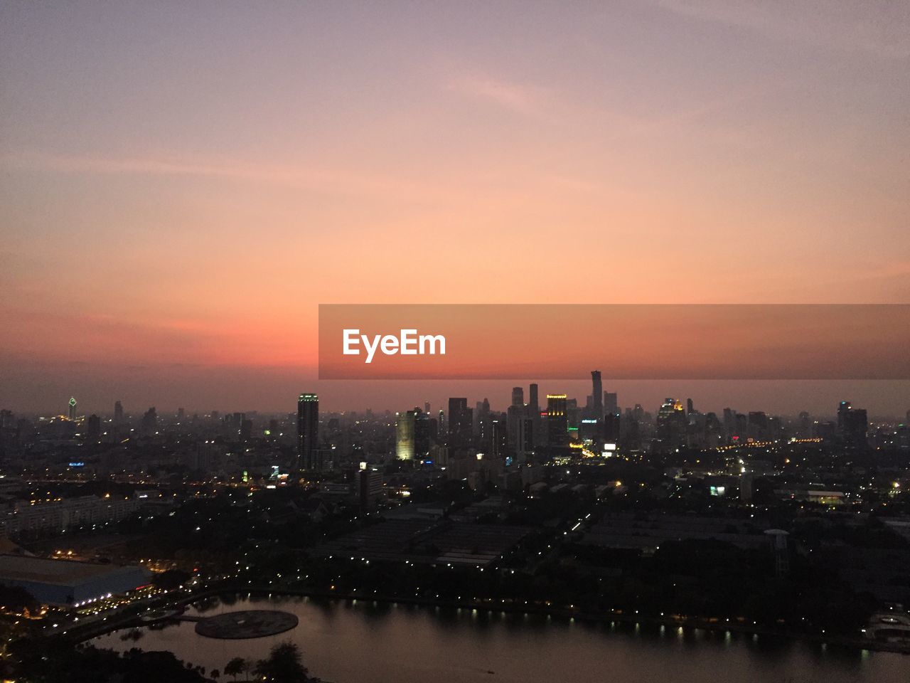 River by illuminated cityscape against sky during sunset