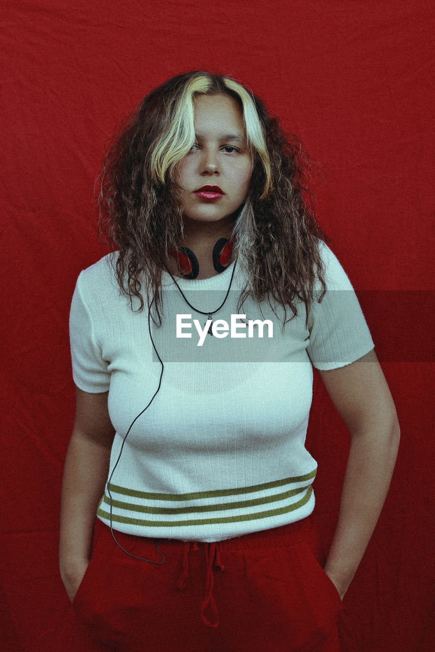 Portrait of young woman standing by red wall