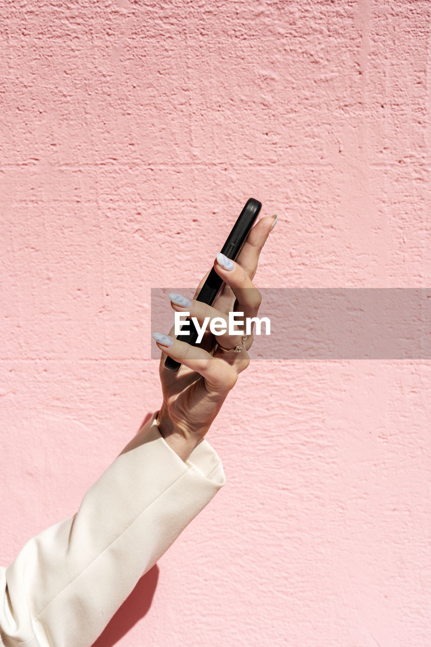 Elegant female hand holding mobile phone at pink background