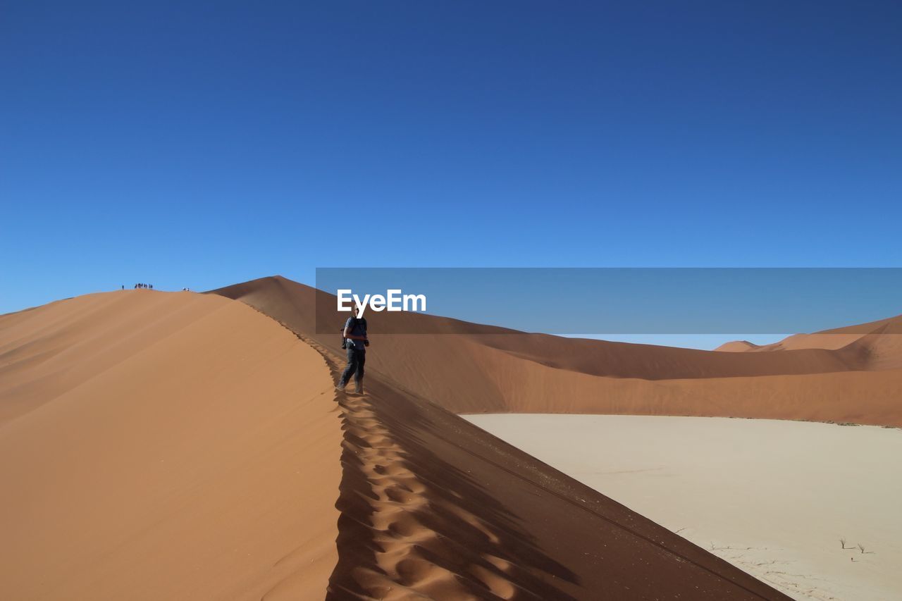 Man standing on sand dune against clear blue sky