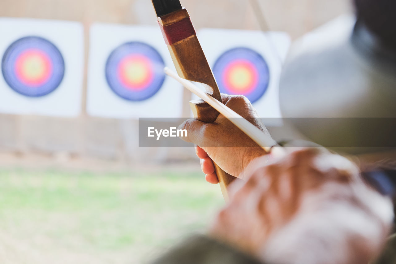 Cropped hands of woman with bow and arrow aiming at target