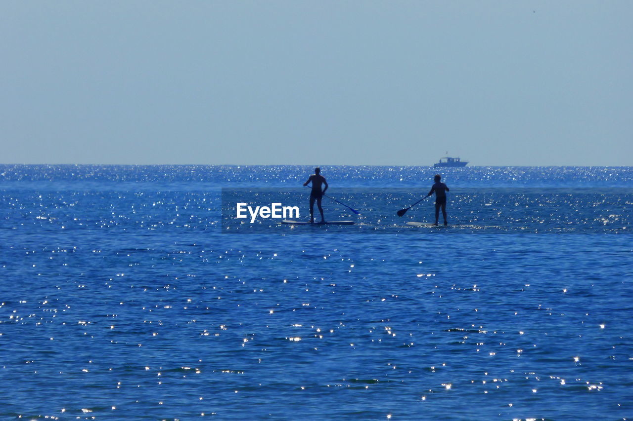 MEN STANDING ON SEA AGAINST CLEAR SKY