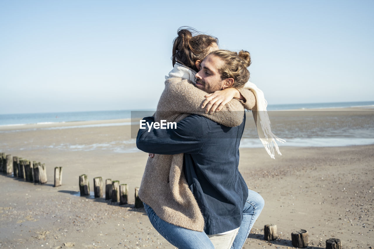 Boyfriend embracing girlfriend while picking up on beach during weekend