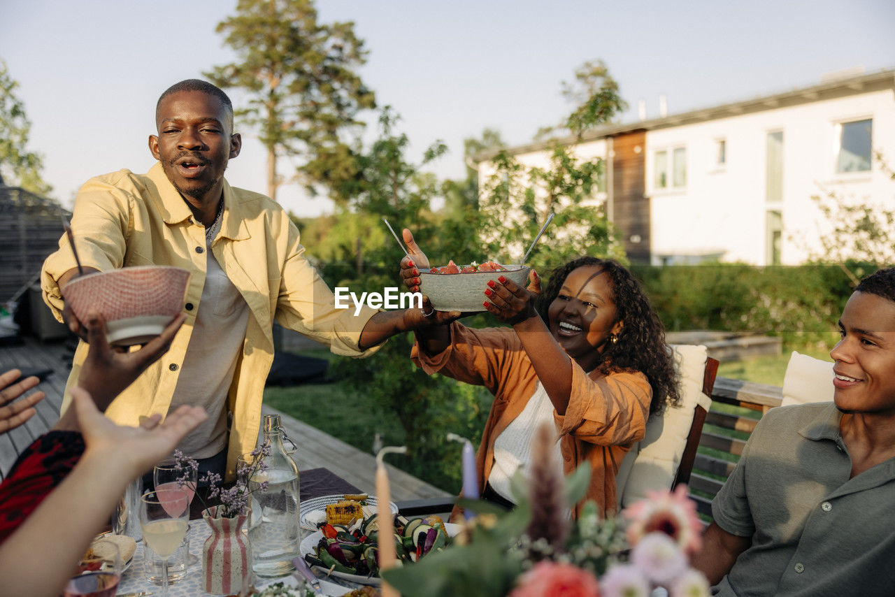 Young man serving food to friends during dinner party in back yard