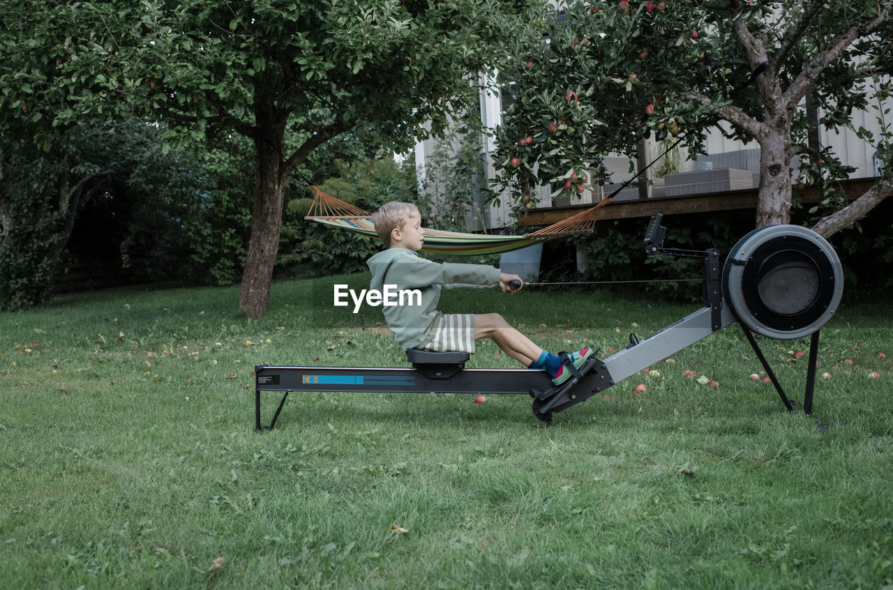 Boy using the rowing machine in his garden at home exercising