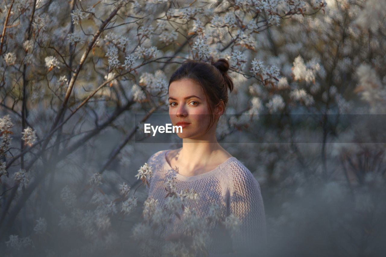 Portrait of young woman standing against trees