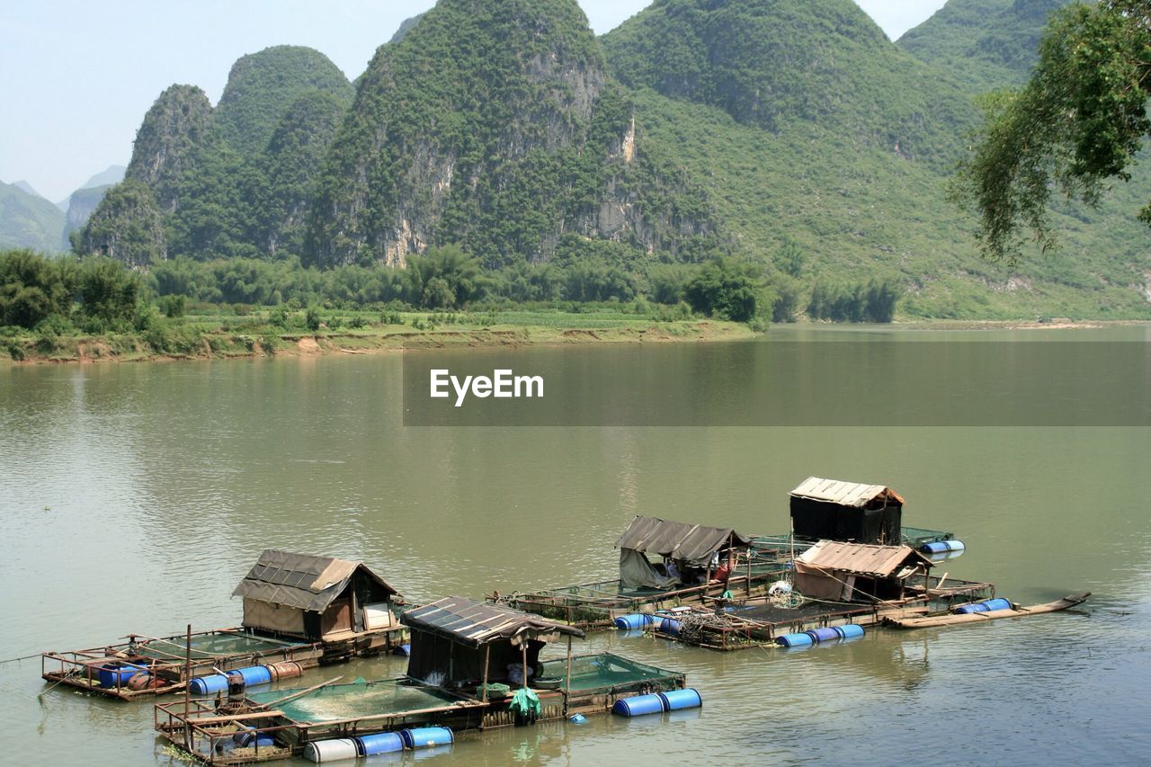 Boat houses floating on water against rocky mountains