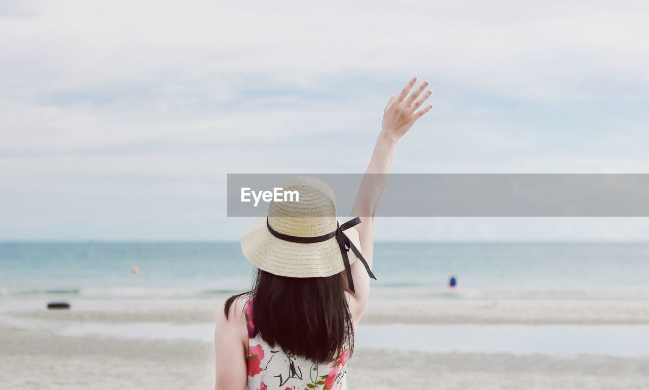 Rear view of woman with arms raised at beach against sky