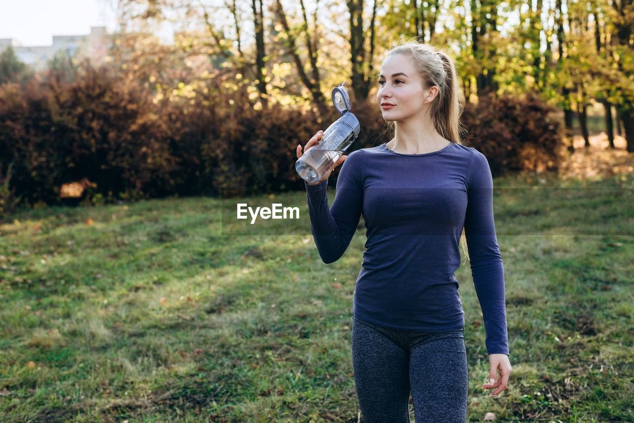 Fitness in the park, girl holds a bottle of water in her hand.