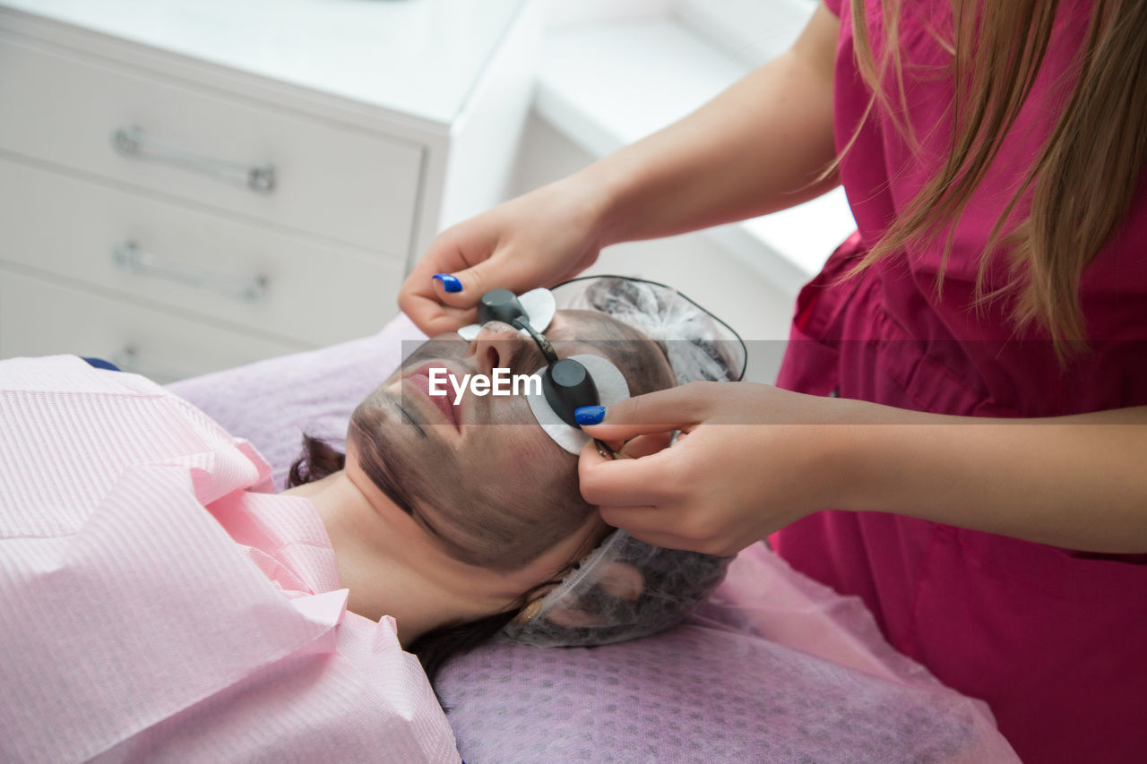 Woman wears protective glasses over cotton pads over her eyes during the carbon peeling procedure.