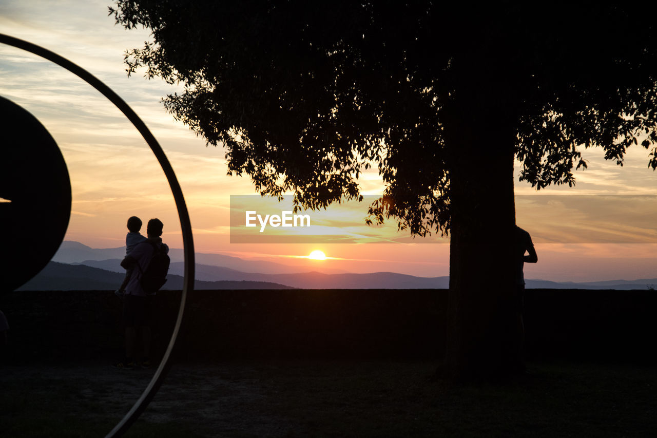 SILHOUETTE PEOPLE STANDING BY TREE AGAINST SKY DURING SUNSET