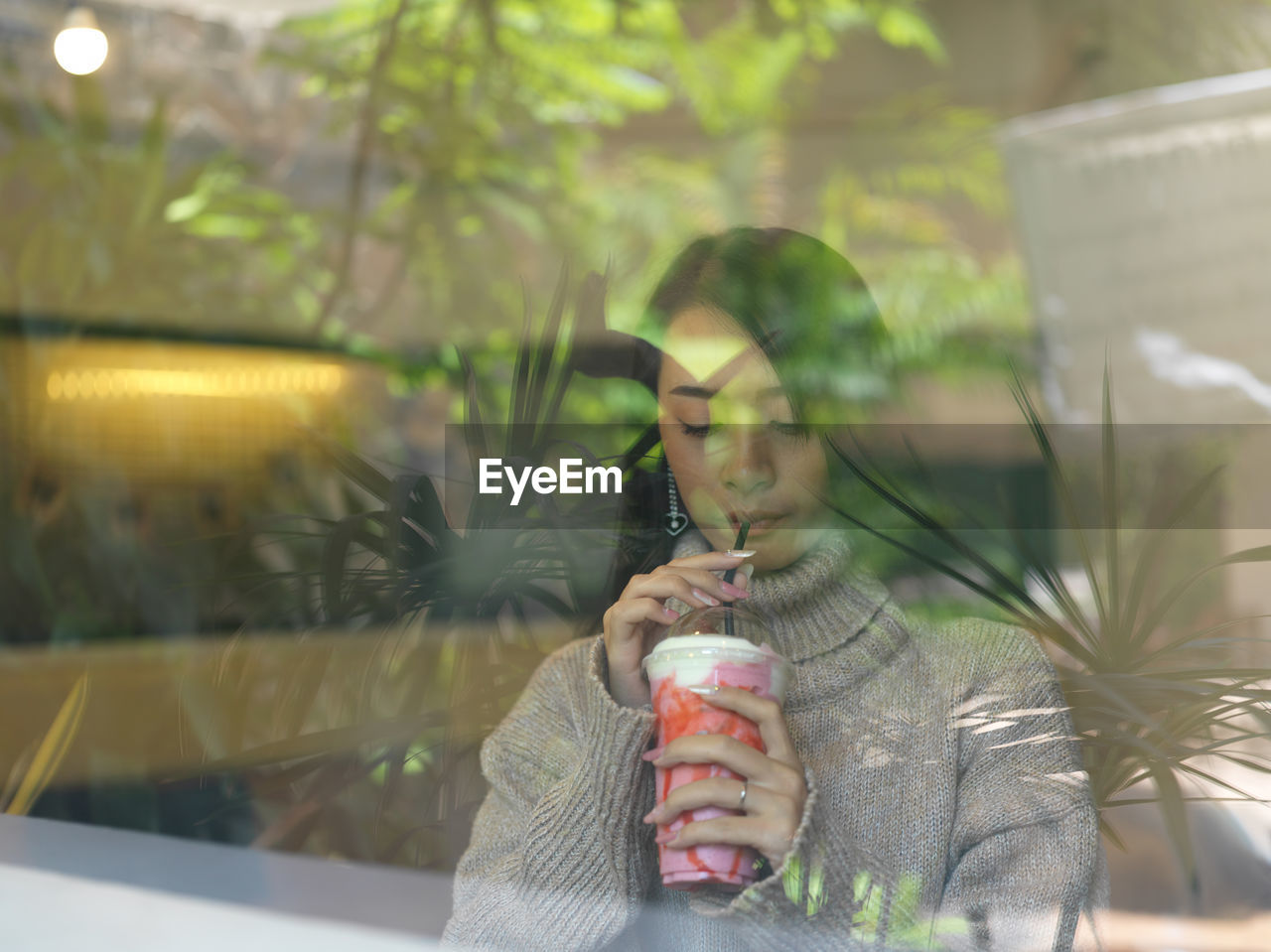 Young woman drinking milkshake seen through glass