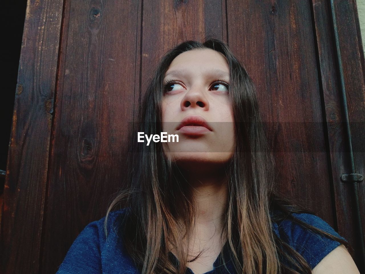 Low angle view of thoughtful woman standing against wooden door