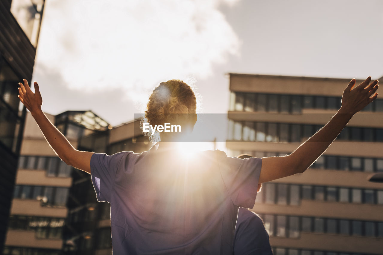 Low angle view of female nurse with arms outstretched standing while facing towards sunlight