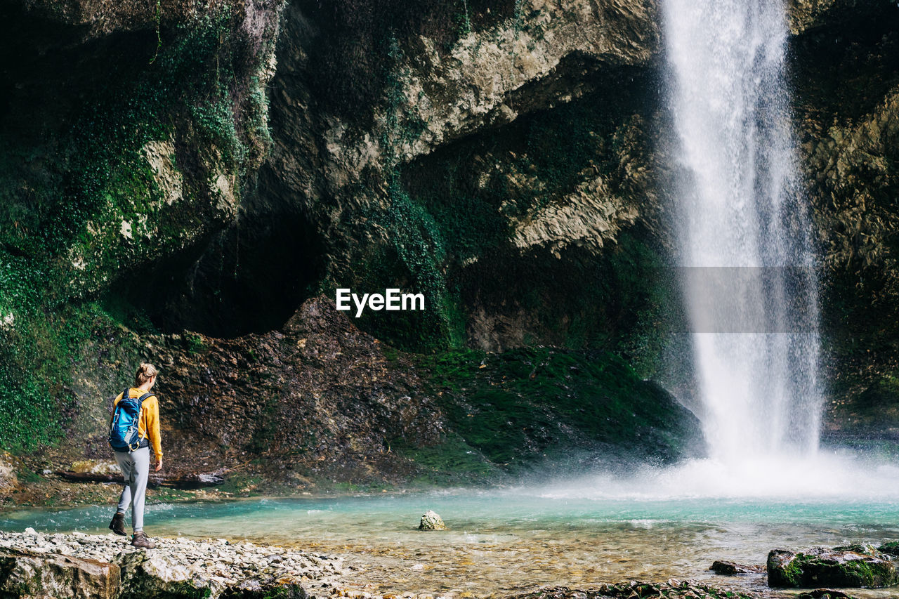 A woman hiker with a backpack in nature walks in a canyon near a waterfall and a stream