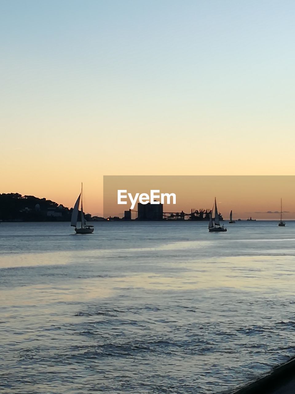 SILHOUETTE BOATS IN CALM SEA AGAINST CLEAR SKY AT SUNSET