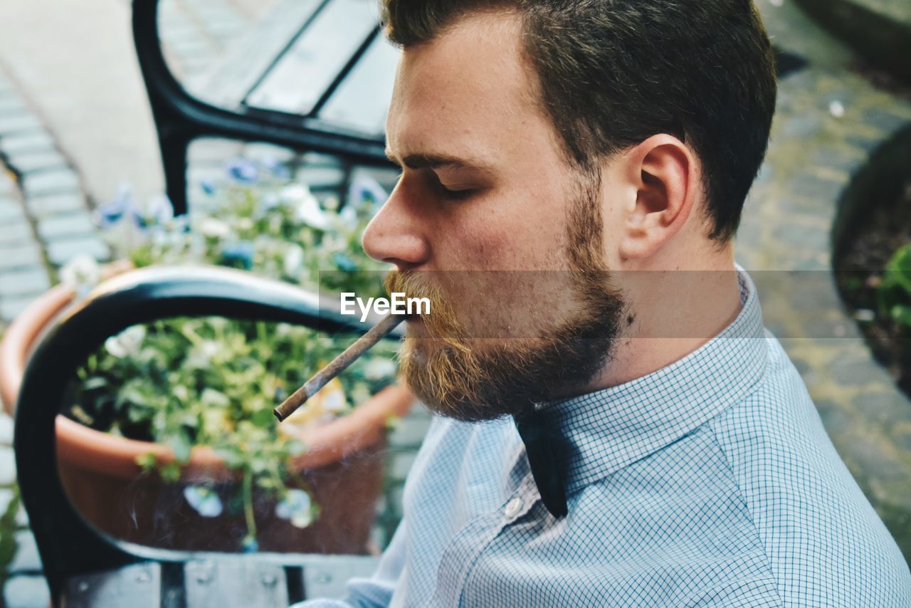 Side view of man with marijuana joint sitting on bench