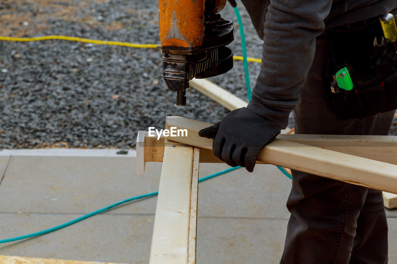 Midsection of man using nail gun on woods at construction site