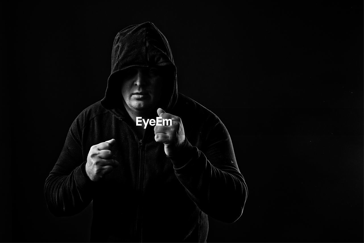 Man wearing hooded shirt standing against black background