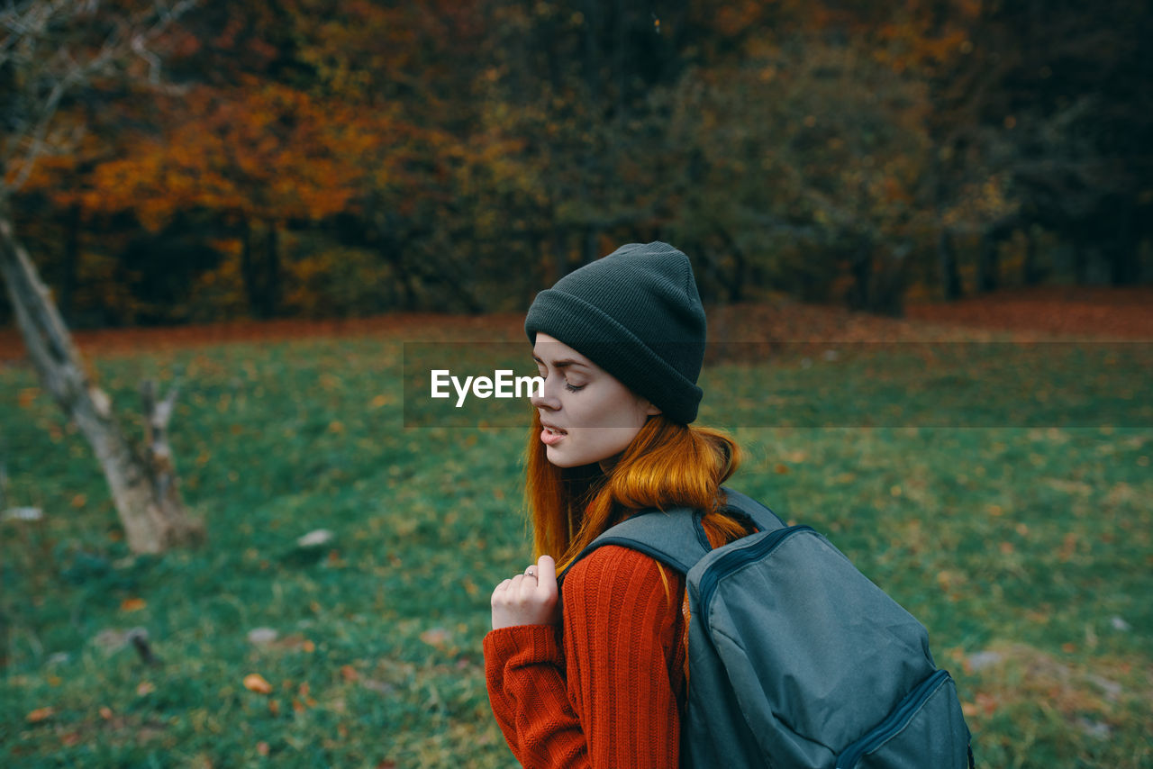 YOUNG WOMAN LOOKING AWAY WHILE STANDING ON TREE