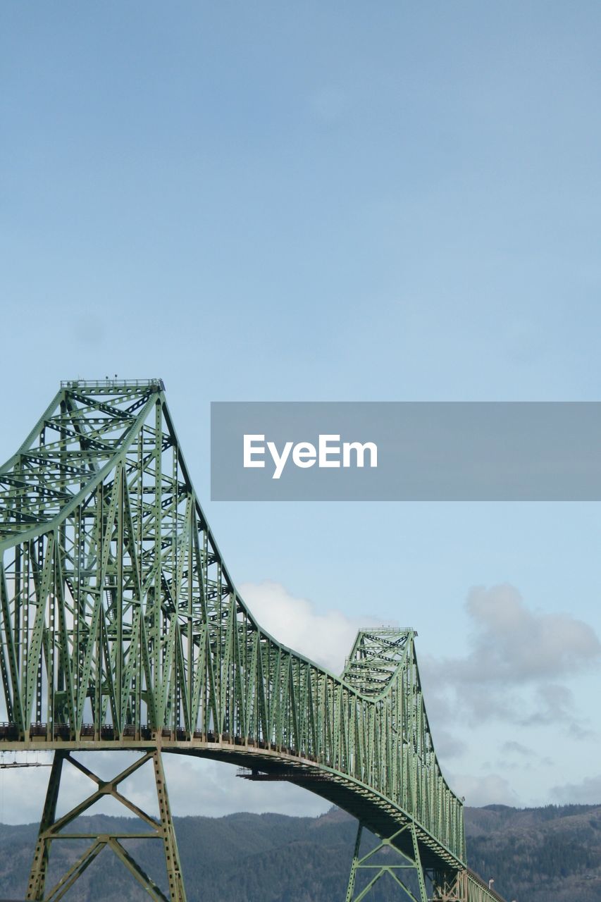 LOW ANGLE VIEW OF BRIDGE AGAINST SKY IN CITY AGAINST CLOUDY DAY