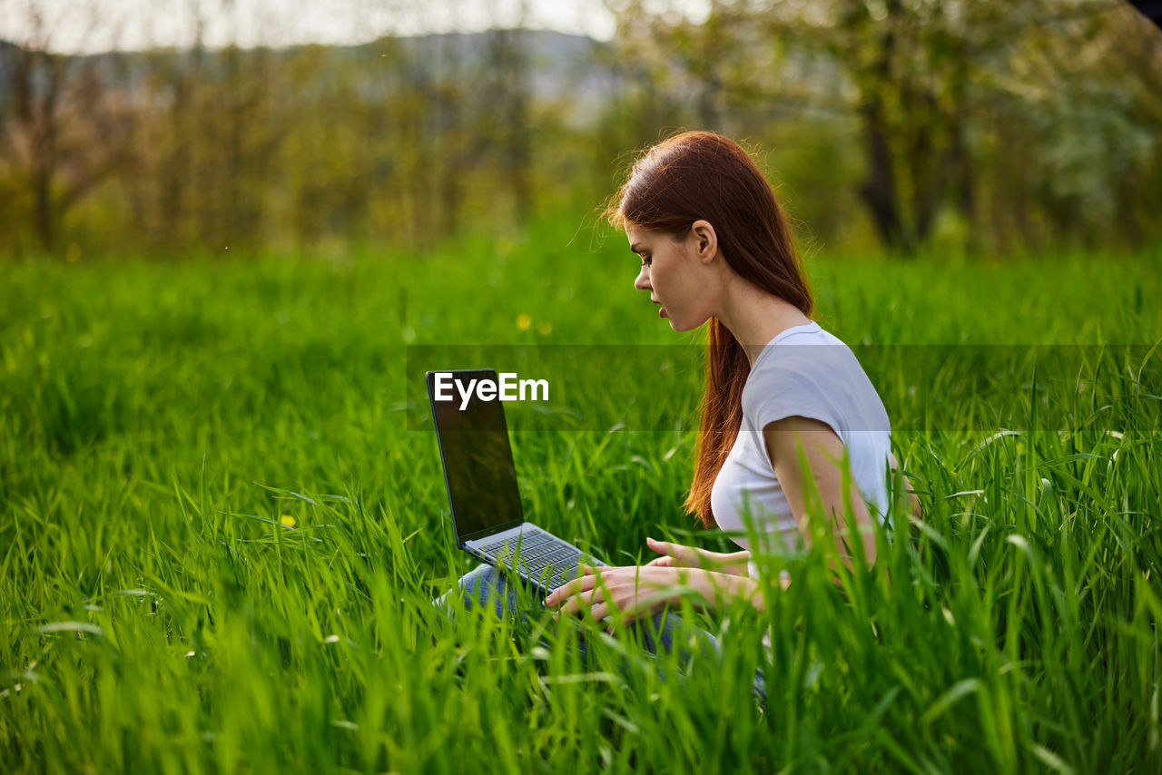 young man using mobile phone while sitting on grassy field